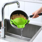 Green silicone clip-on strainer on a pot draining pasta over a kitchen sink