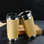 Two bamboo travel coffee cups with black lids on a dark table next to a wooden tray