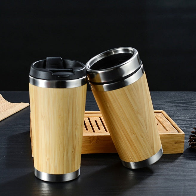 Two bamboo travel coffee cups with black lids on a dark table next to a wooden tray