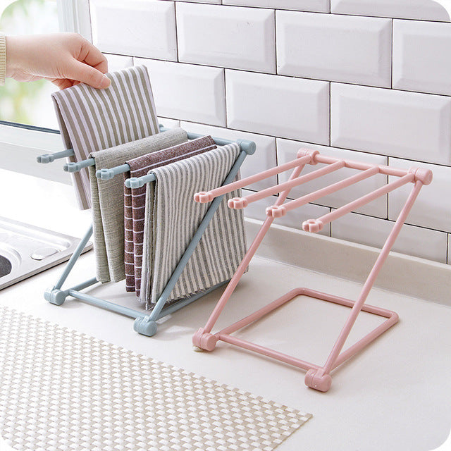 Pink folding rack on a kitchen counter holding several dish cloths and towels
