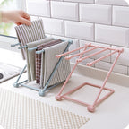 Pink folding rack on a kitchen counter holding several dish cloths and towels