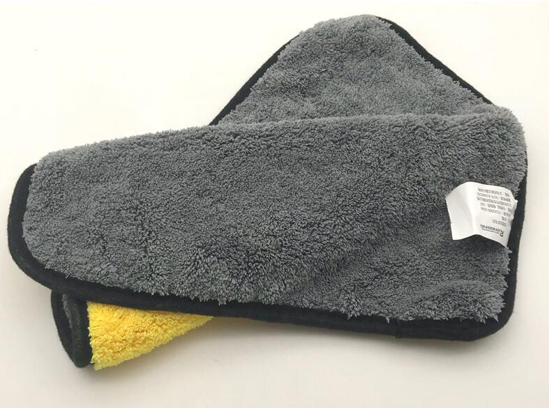 Hand wiping a car mirror with a yellow and grey cleaning towel