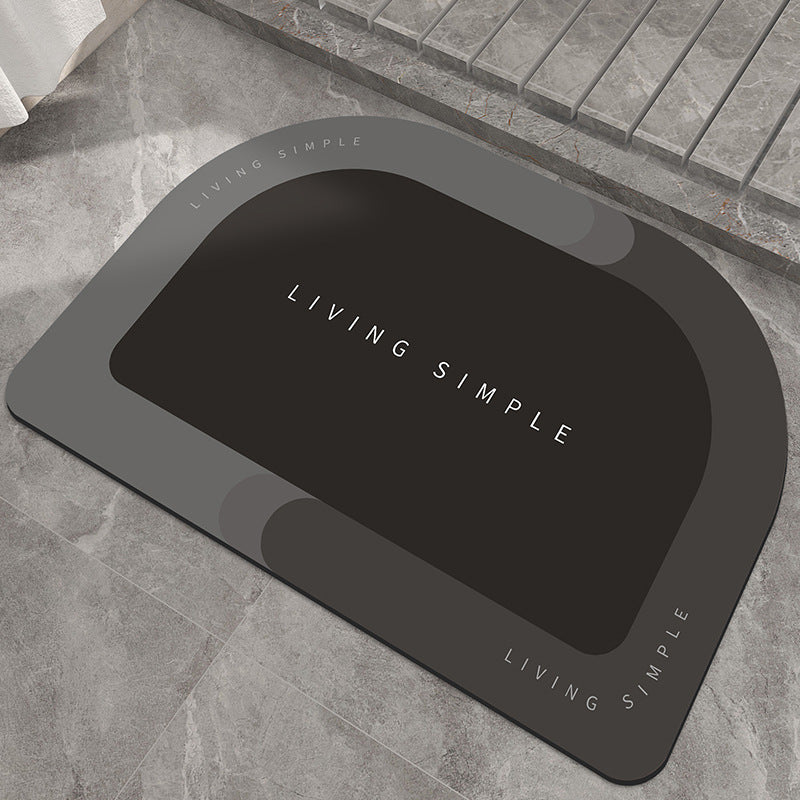 Charcoal grey oval bath mat with a black centre on a stone floor
