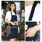 Black apron worn by a woman, with a close-up of the front pocket and neck strap