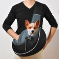 Person wearing a black pet sling carrier with a small brown and white dog looking out