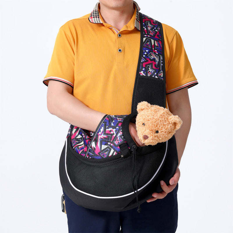 Person in an orange shirt wearing a black sling carrier with a patterned strap and holding a plush toy