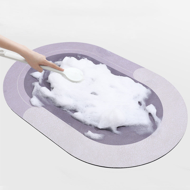 Purple-grey oval bath mat seen from above with a hand pressing soapy foam onto its surface