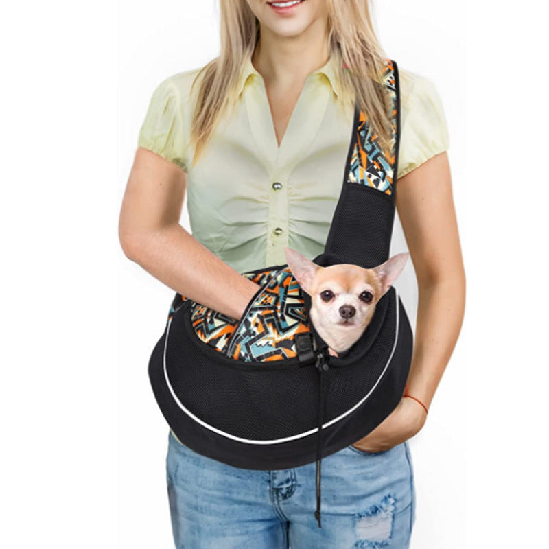 Woman wearing a black sling carrier with a patterned strap and a small dog inside