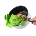 Green clip-on strainer attached to the rim of a pot while pouring out water and noodles