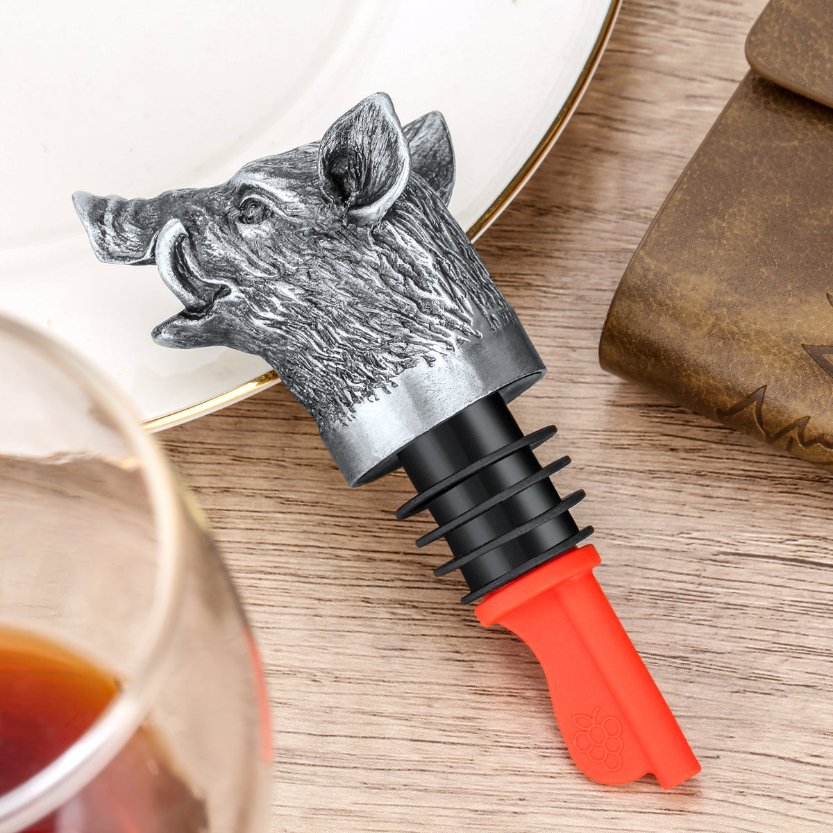Dark Silver wild boar head wine pourer on a plate beside a glass